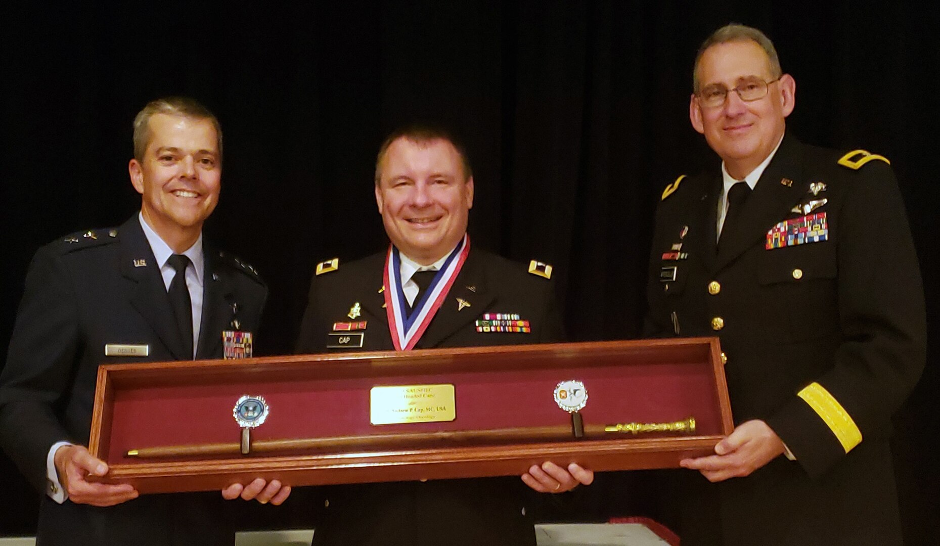 Air Force Maj. Gen. John DeGoes (left), 59th Medical Wing commander, and Army Brig. Gen. George Appenzeller (right), Brooke Army Medical Center commanding general, present the 2019 Gold Headed Cane Award to Army Col. (Dr.) Andrew Cap, chief of coagulation and blood research at the U.S. Army Institute of Surgical Research, during the San Antonio Uniformed Services Health Education Consortium awards dinner May 18 at the Parr Club at Joint Base San Antonio-Randolph. The Gold Headed Cane Award focuses on four areas: patient care, resident teaching, clinical research and operational medicine.