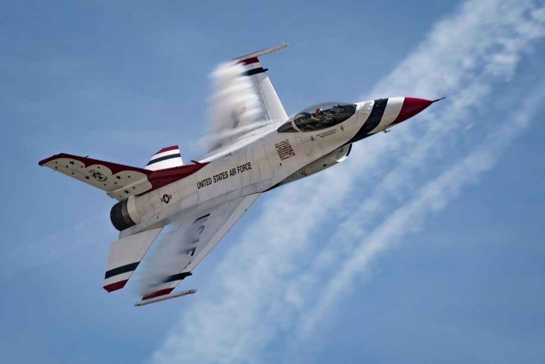 A fighter jet’s wings cut through vapor in a blue sky.