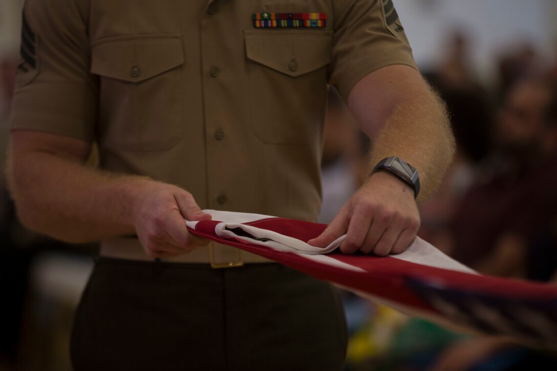 A U.S. Marine performs the “13 Folds” during Command Master Chief Petty Officer Russell Folley’s retirement ceremony on Camp Lejeune, N.C., May 24, 2019. Folley, a St. Martinville, Louisiana native, is retiring after 33 years of service in the U.S. Navy. Folley described one of the favorite things in his career was watching both Marines and junior Sailors succeed. He added at the end of his speech during the ceremony that his best moments in the Navy were while wearing Marine pattern utilities. (U.S. Marine photo by Cpl. Leynard Plazo)