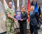 Event guest speaker being presented a memento of appreciation by two members of DLA Land and Maritime command staff.