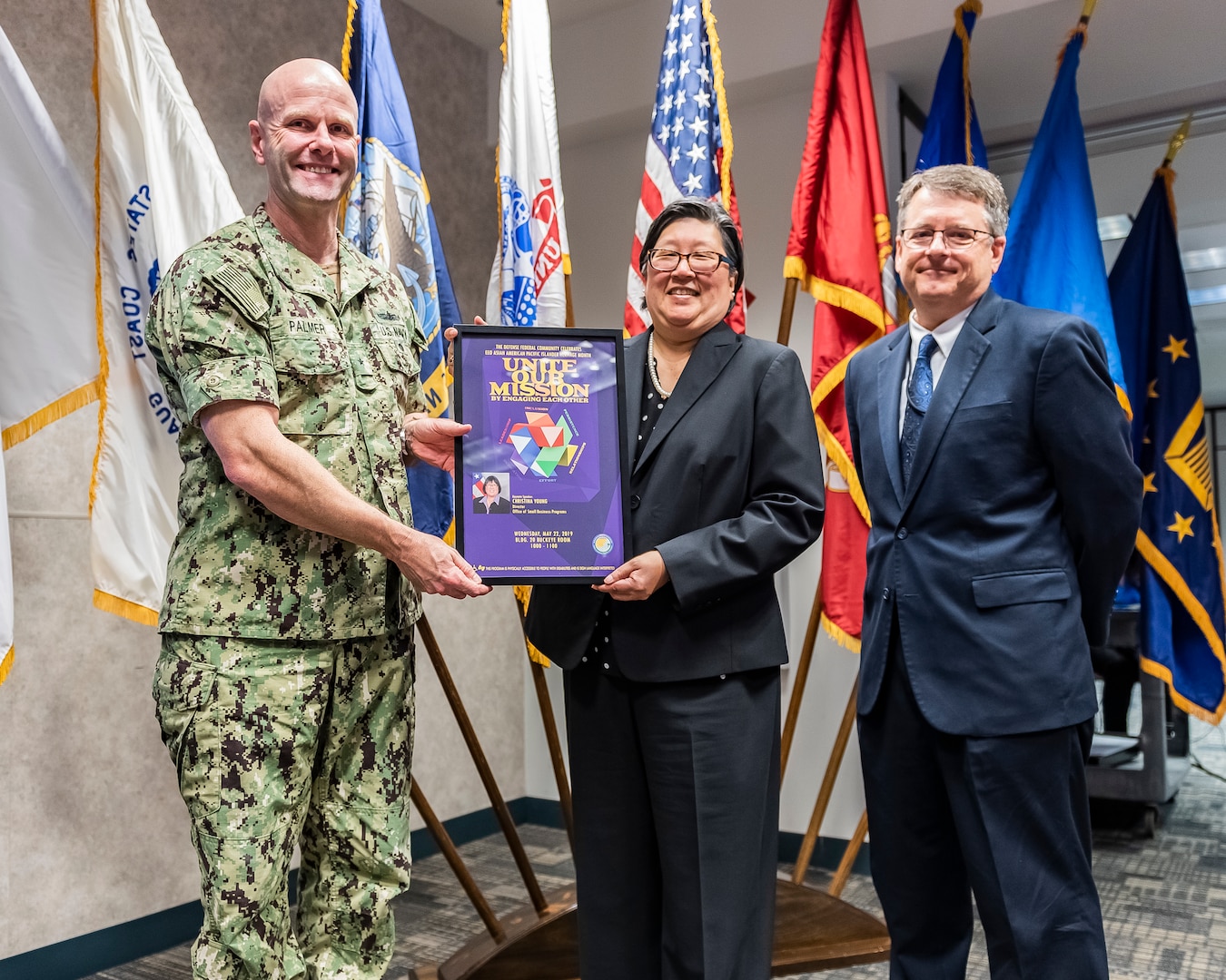 Event guest speaker being presented a memento of appreciation by two members of DLA Land and Maritime command staff.