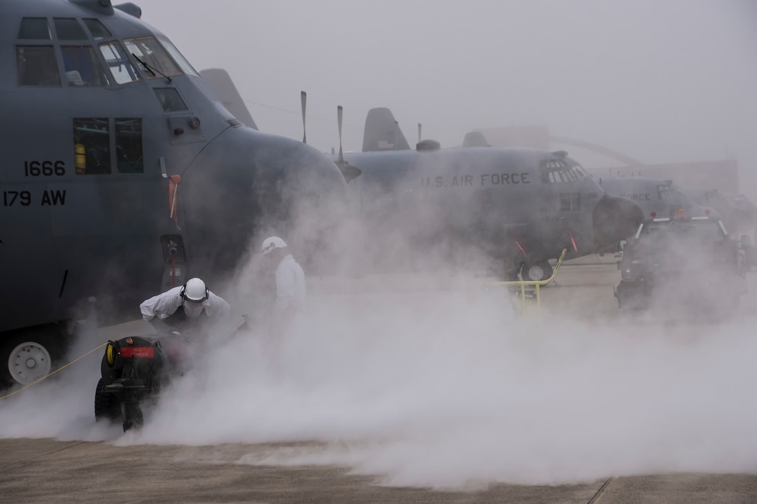 Airmen fill liquid oxygen tanks for military aircraft in foggy conditions.