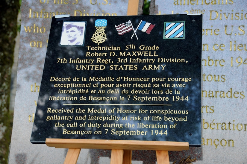 A plaque honoring a soldier sits on an easel in front of a monument.