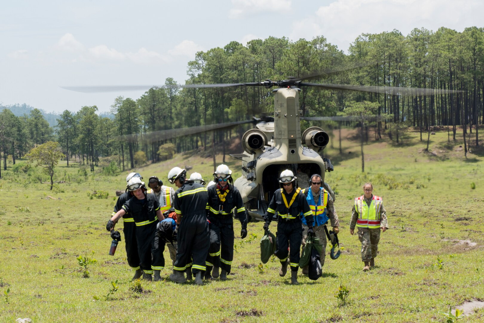 A group of 612th Air Base Squadron firefighters carry equipment from a CH-47 Chinook to the site of a simulated aircraft crash during a search and rescue exercise, May 21, 2019, in Comayagua, Honduras. Members from various units on Joint Task Force – Bravo participated in the exercise that simulated a HH-60 Blackhawk crashed during a routine flight carrying personnel. The exercise practiced notification, recall, search and rescue, on-scene medical care, recovery of personnel from low and high angle austere terrain, and medical care once the injured returned to base. (U.S. Air Force photo by Staff Sgt. Eric Summers Jr.)