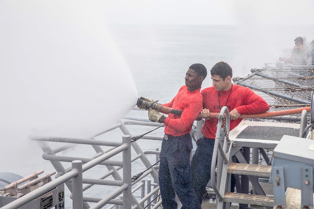 Two sailors test a foam system on a ship.