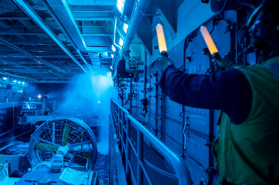 A sailor uses to light sticks to signal towards an air-cushioned landing craft.