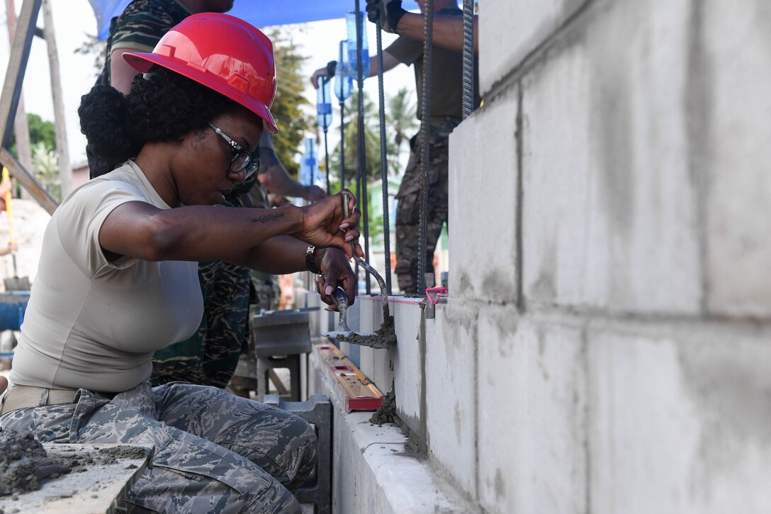 An airman holding a trowel reinforces brickwork on a community center.