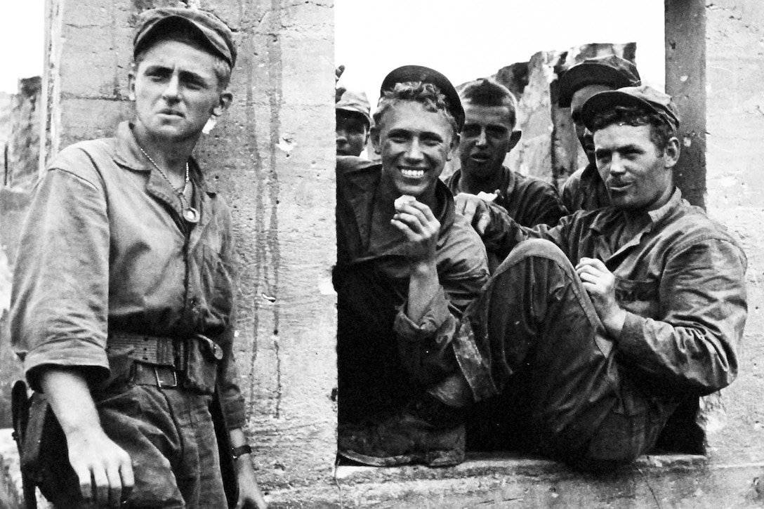 Marines smile and pose for a photo by a cement-type wall.