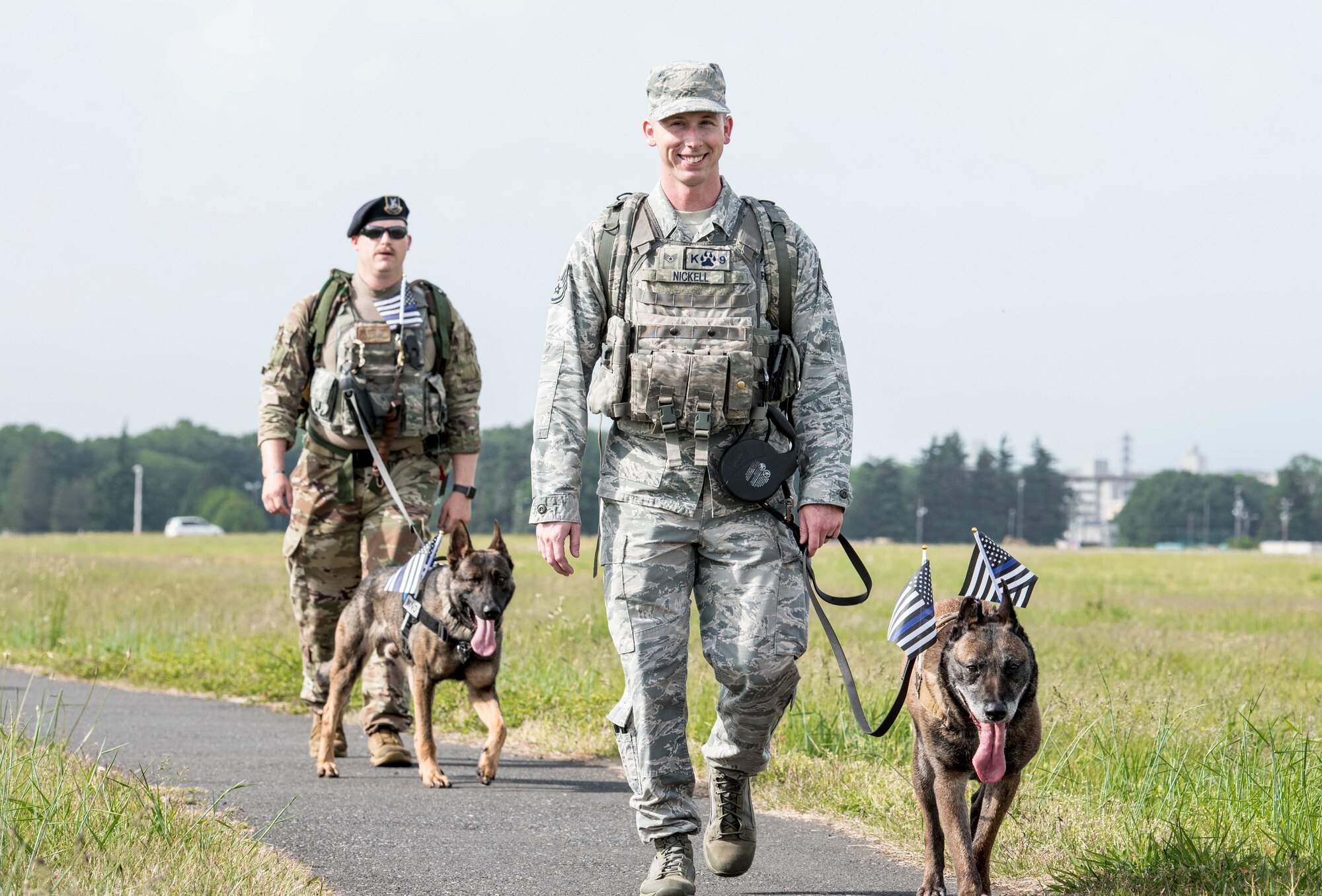 (Front to back) Staff Sgt. Cody Nickell and Staff Sgt. David Ferro, both 374th Security Forces Squadron military working dog handlers, walk along the sidewalk with their dogs during Yokota’s 2019 National Police Week 5K Ruck March, May 20, 2019, at Yokota Air Base, Japan.