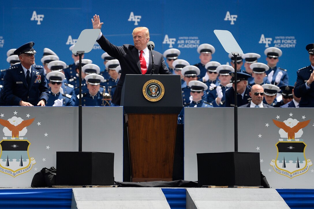 President Donald J. Trump waves to an audience from behind a podium.