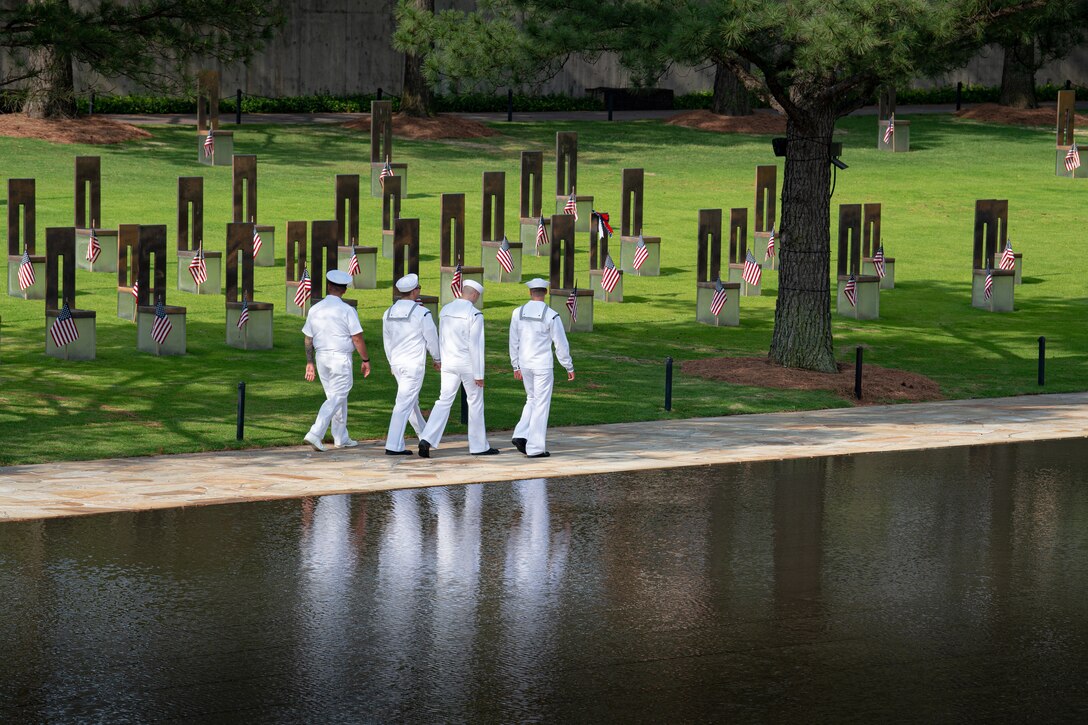 Four sailors walk beside a pool of water.