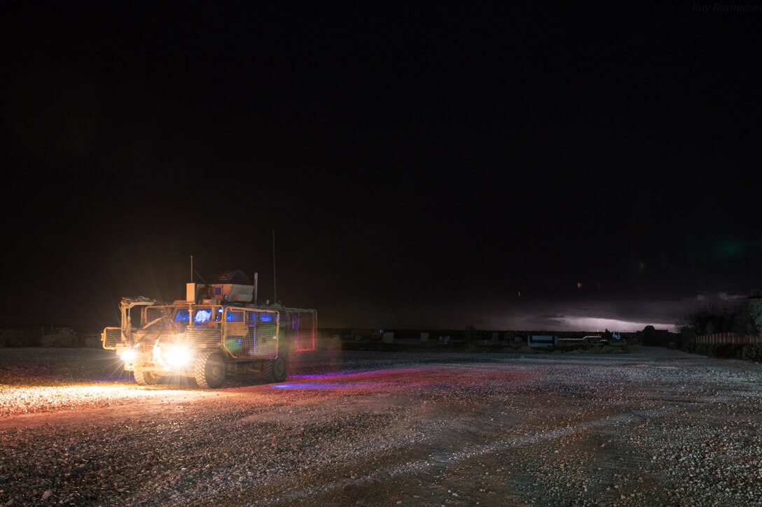 A military combat vehicle moves across a gravel yard in the dark of night.