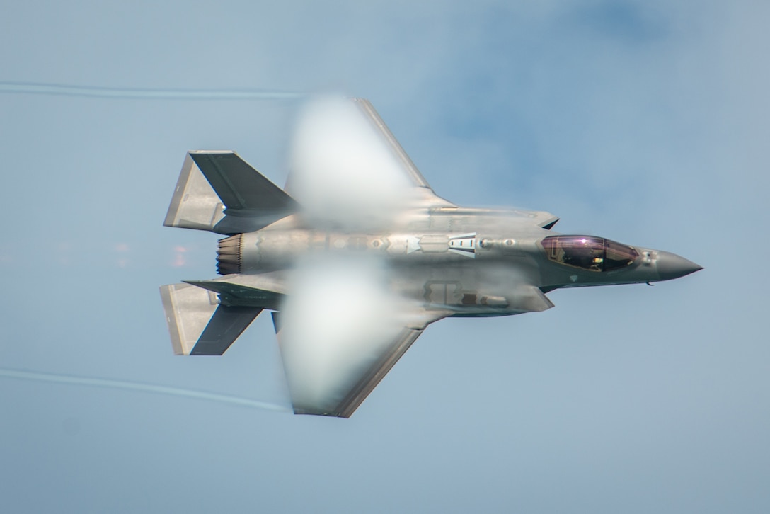 Vapor covers the wings of a fighter jet as it streaks through the sky.