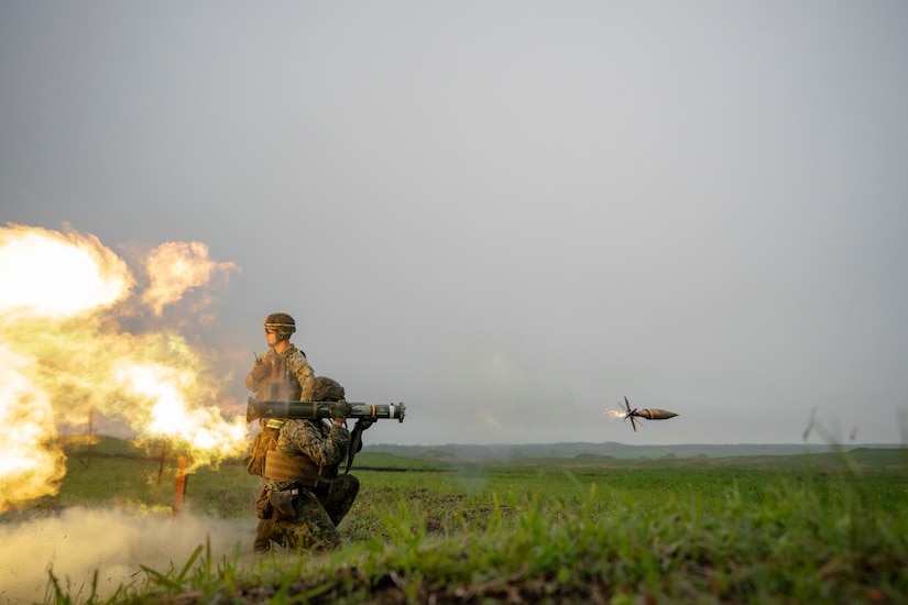 A Marine fires a shoulder-launched rocket while another looks on.