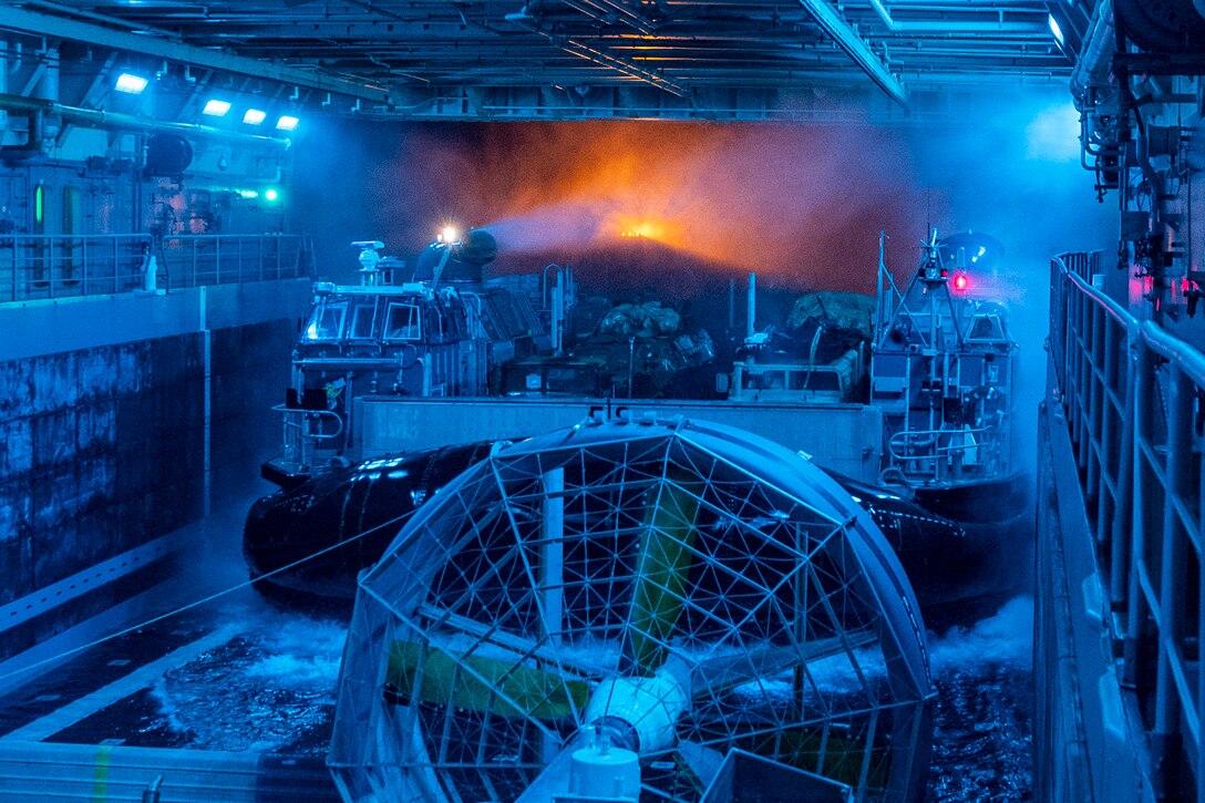 An air-cushioned landing craft enters the well deck of a ship bathed in blue light.