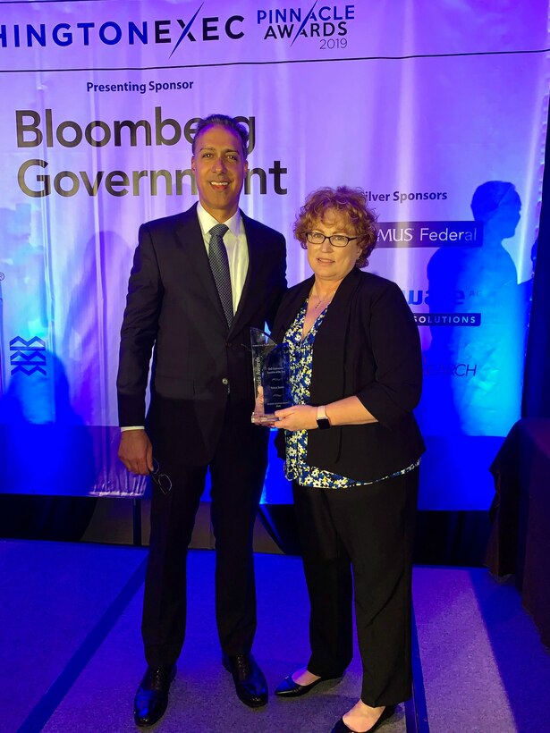 Teresa Smith and a WashingtonExec official stand on a stage holding an award