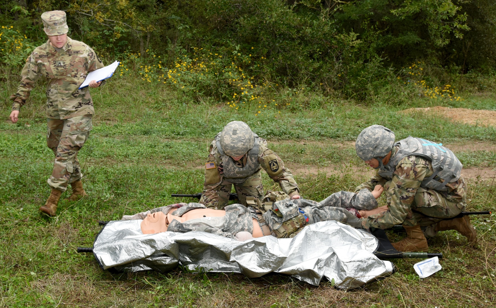 Staff Sgt. Rachel Hammill (center) and Cpl. Christopher Olverson prepare a wounded Soldier for medical evacuation as Sgt. Claudia Napier, lane non-commissioned officer in charge, observes and evaluates the assigned task. The U.S. Army Institute of Surgical Research at Joint Base San Antonio-Fort Sam Houston conducted Army Warrior Training at Salado Creek Training site at JBSA-Fort Sam Houston Oct. 23-24.