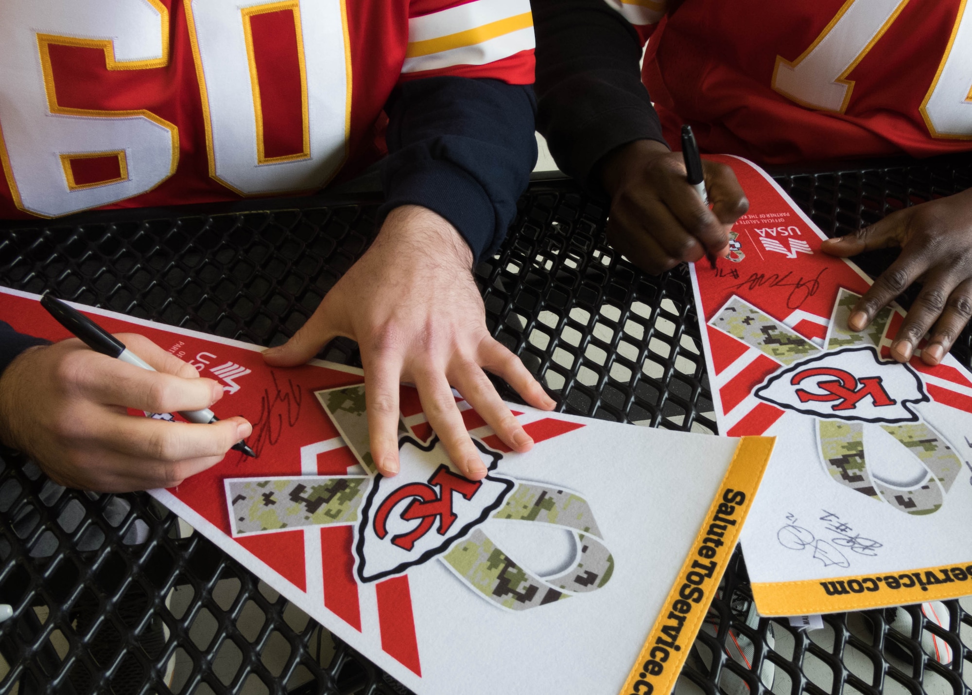 National Football League’s Kansas City Chiefs offensive linemen Ryan Hunter, #60, and Greg Senat, #70, autograph Salute to Service flags during a meet-n-greet on the flightline at Whiteman Air Force Base, Missouri, Oct. 29, 2019.