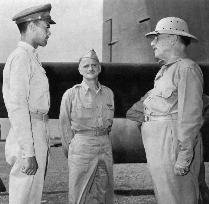 Two men in uniform meet a man in civilian clothes and a pith helmet.
