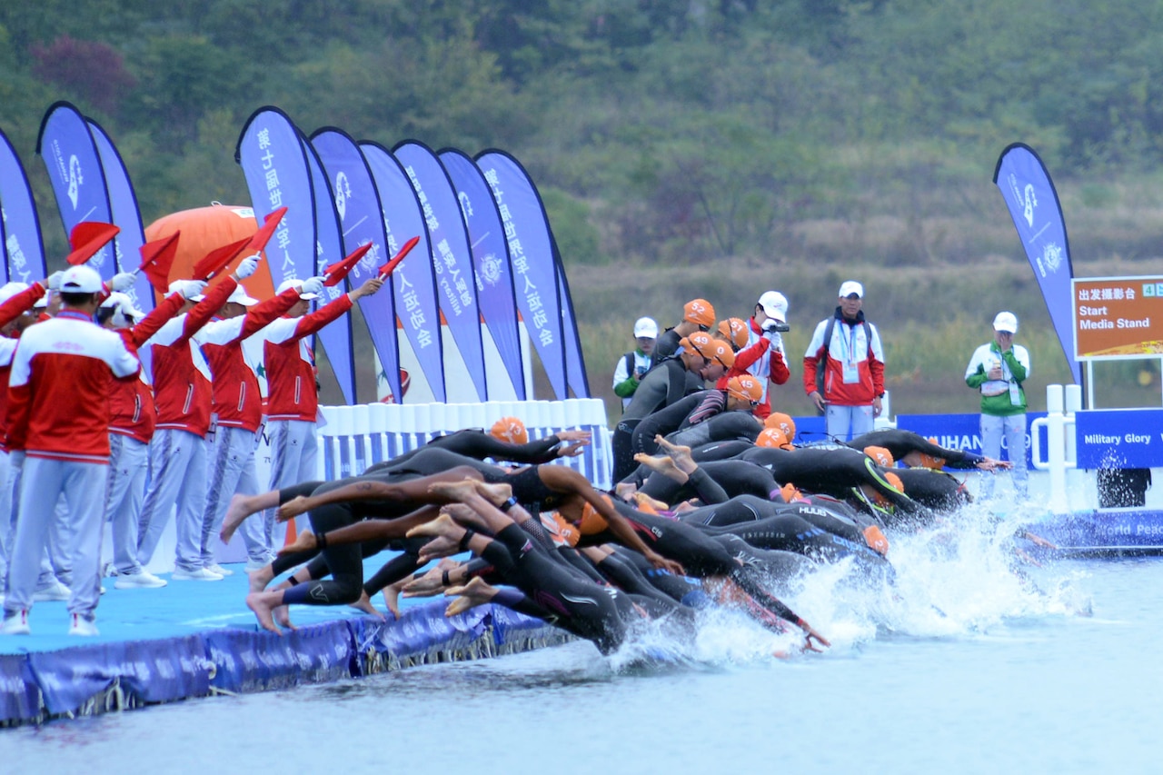 Swimmers dive into a pool to begin the swimming portion of a triathlon competition.