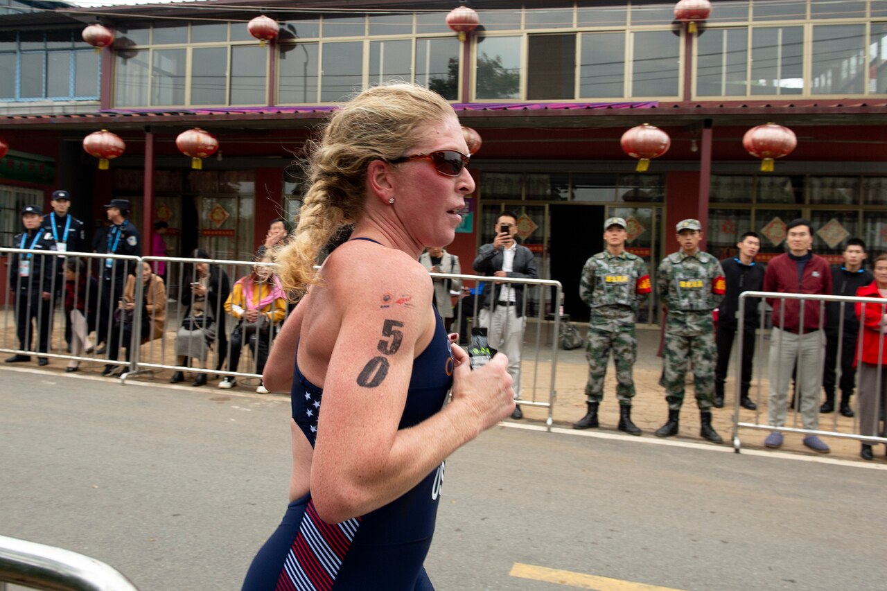 Woman triathlon athlete runs with “50” on her right arm.