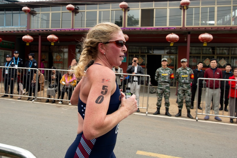 Woman triathlon athlete runs with “50” on her right arm.
