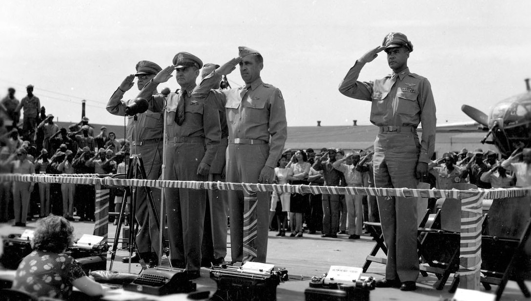 A group of service members salutes while standing on an elevated platform.