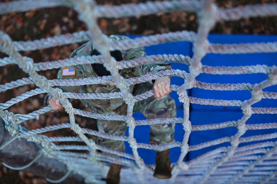 A soldier climbs a rope wall.