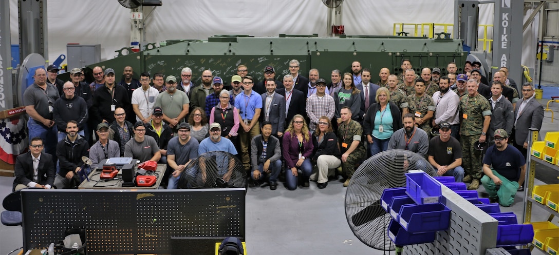 Representatives from Program Manager Advanced Amphibious Assault at Program Executive Officer Land Systems, Marine Corps Combat Development Command, Combat Development and Integration and 3rd Assault Amphibian Battalion pose in front of an unfinished Amphibious Combat Vehicle with the manufacturing workforce in York, Pennsylvania, on Oct. 16, 2019.