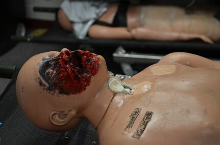 Ground charcoal is added to the red paint on the face of the manikin to create a realistic facial wound.  Moulage transforms low-fidelity manikins into combat casualties to simulate battlefield wounds or injuries to train combat medics.