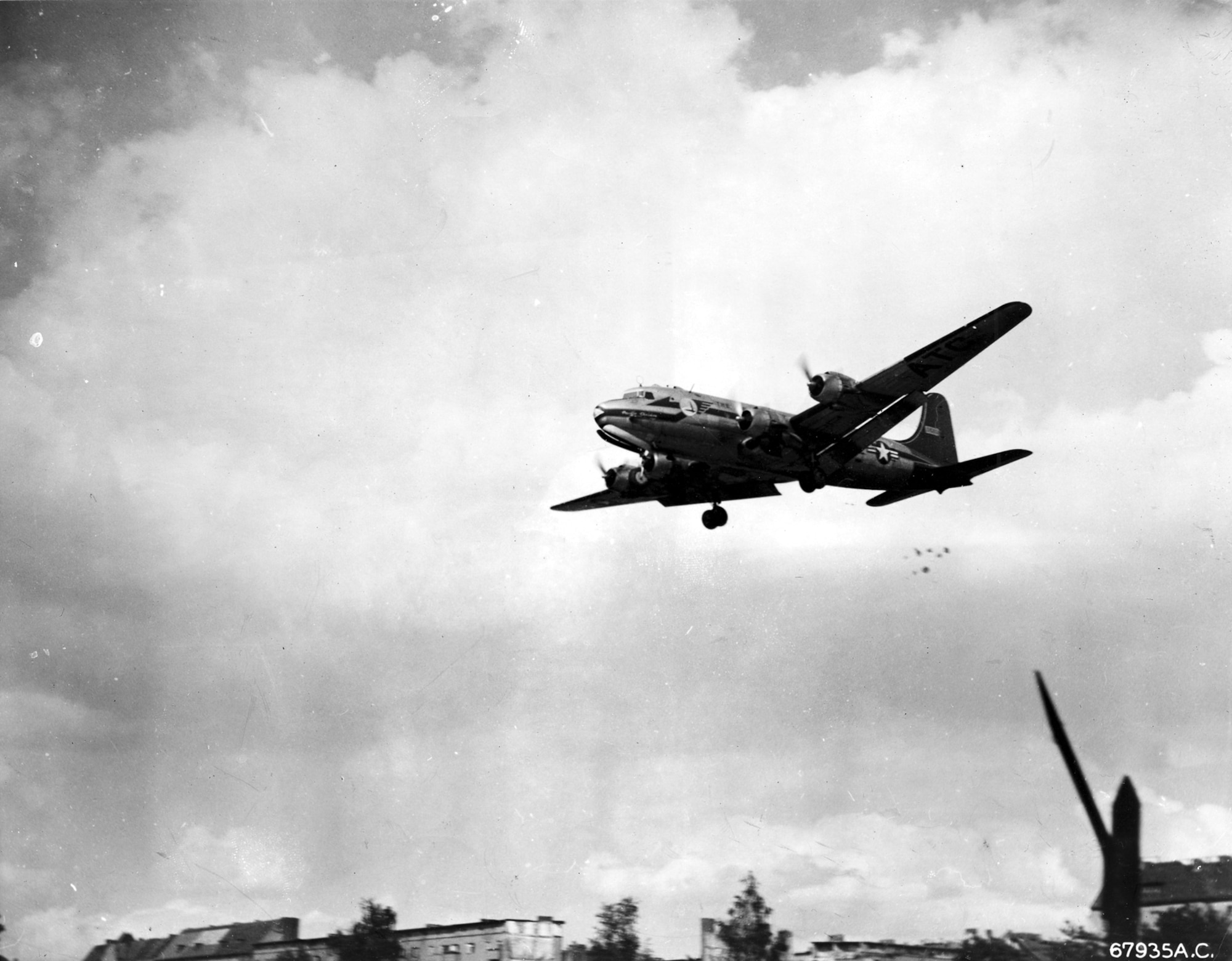 A C-54 piloted by retired Col. Gail Halvorsen drops candy with attached parachutes to children during the Berlin Airlift. Halverson earned the nickname “Candy Bomber” for his "Little Vittles" candy drops. Note the parachutes below the tail of the C-54. (U.S. Air Force photo)