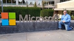 Man poses beside Microsoft sign.