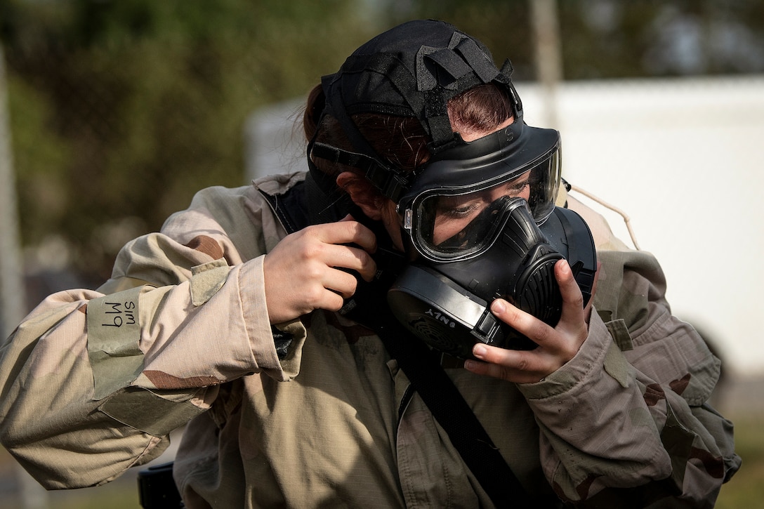 An airman puts on a gas mask outside.