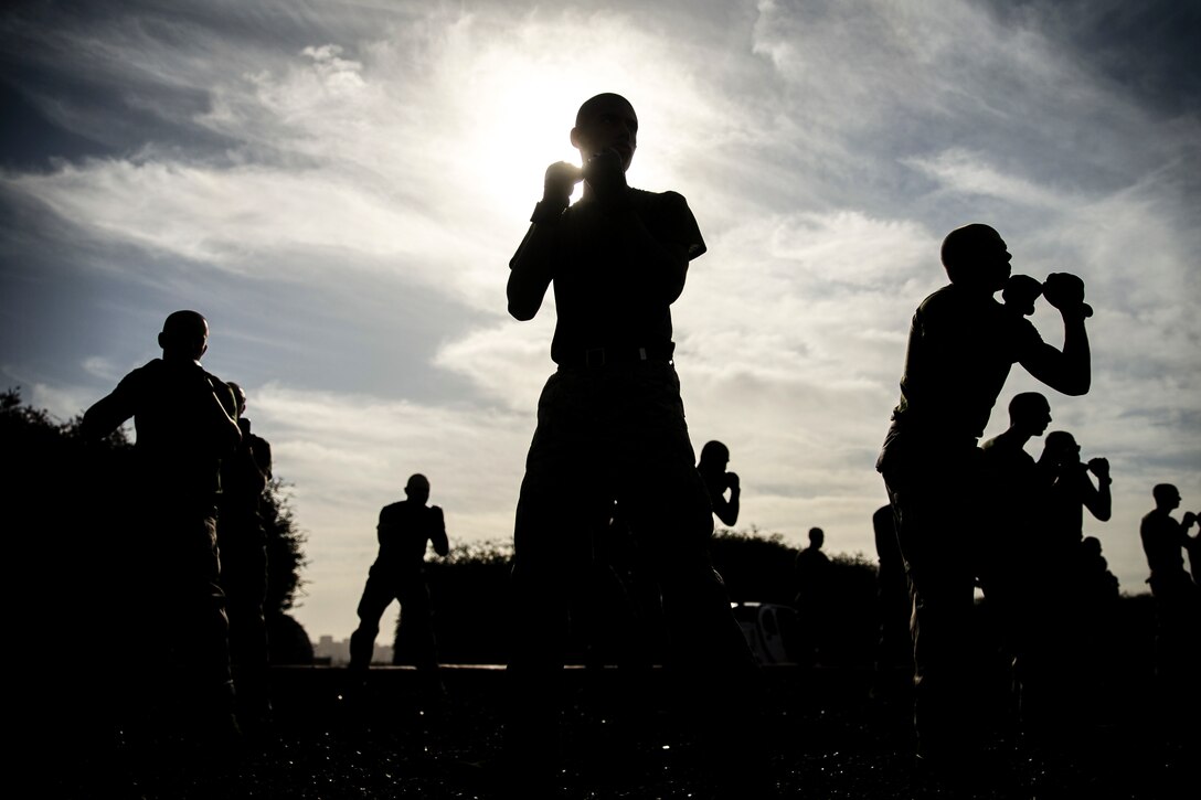 Marines, shown in silhouette, hold their fists up in an outdoor area.