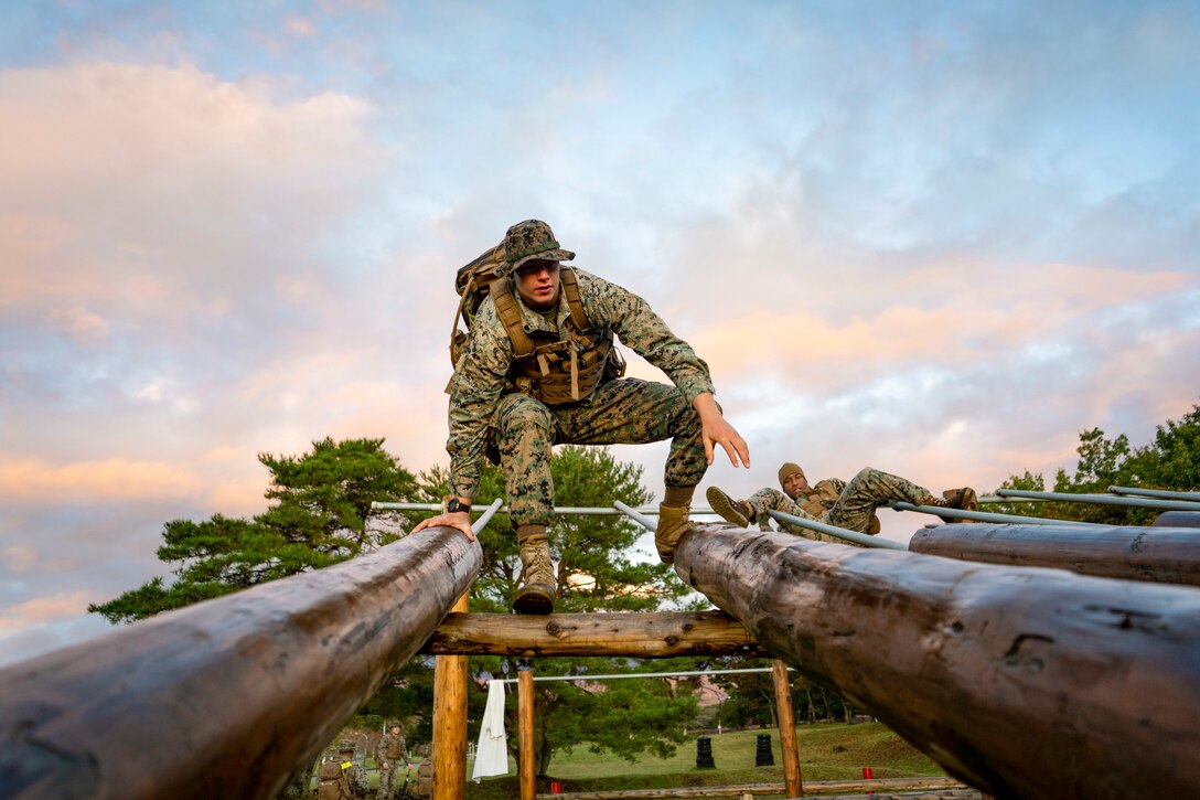 A Marine balances on two horizontal logs elevated off the ground.