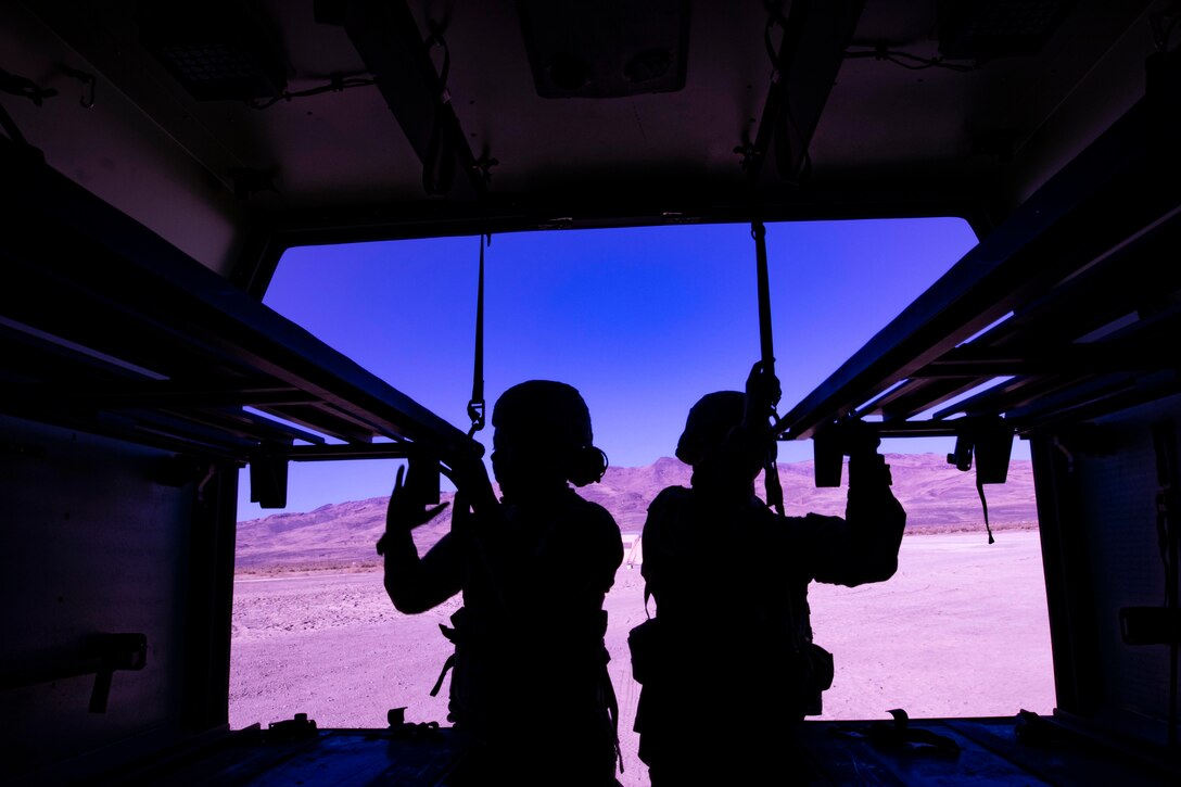 A silhouette of two soldiers standing at the back of a ambulance with mountains in the background.