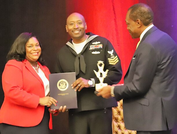 IMAGE: NORFOLK, Va. (Oct. 29) – Hampton Roads Diversity and Inclusion Consortium (HRDIC) leaders present U.S. Navy Information Systems Technician 1st Class Tyrell Hardison with the Pride Service Award certificate and trophy at a luncheon ceremony. Hardison was one of six awardees recognized at the event for exemplifying diversity and inclusion while serving in the armed forces. "The Pride Service Award, which we presented to these community leaders, is the first of its kind in our 10 year history," said Mr. Billy McIntyre, HRDIC chairman of the board. "Today's award recipients have distinguished themselves as leaders and role models in the community and have promoted inclusion in an outstanding manner." Left to right: Aleea Slappy Wilson, the Diversity, Equity and Inclusion officer for the city of Norfolk; Hardison; and McIntyre.