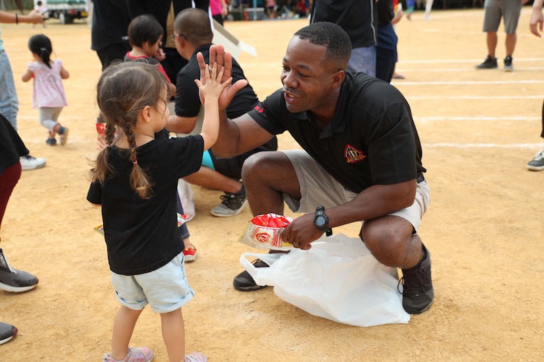 Sgt. Maj. Russell Boley, sergeant major for 2nd Battalion, 2nd Marine Regiment, gives a high-five to a local toddler during the 46th Henoko Sports Festival at Henoko athletic field Nov. 3, 2019, Camp Schwab and Okinawa Defense Bureau were invited to participate in the event.