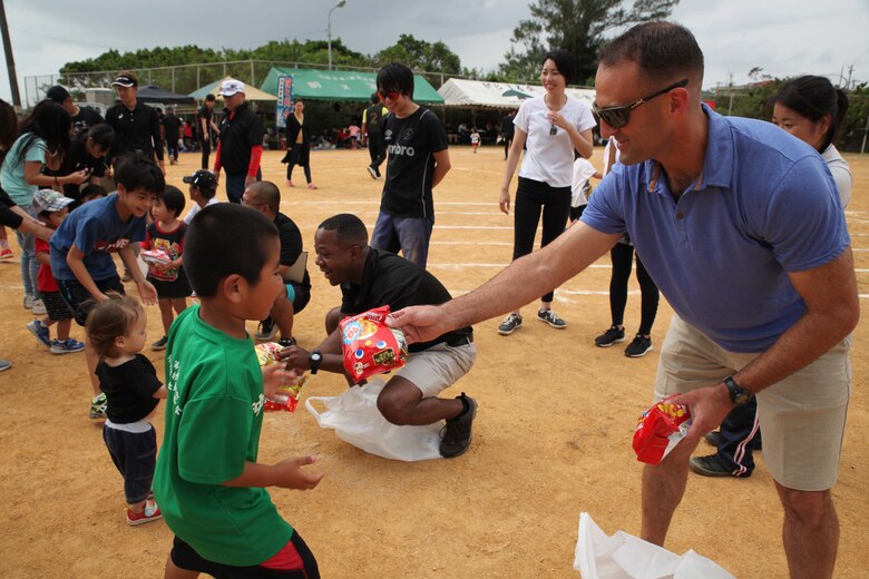 Lt. Col. Stephan Scott, commanding officer, 2nd Battalion, 2nd Marine Regiment, hands a prize to a local child during the 46th Henoko Sports Festival at Henoko athletic field Nov. 3, 2019, Camp Schwab and Okinawa Defense Bureau were invited to participate in the event.