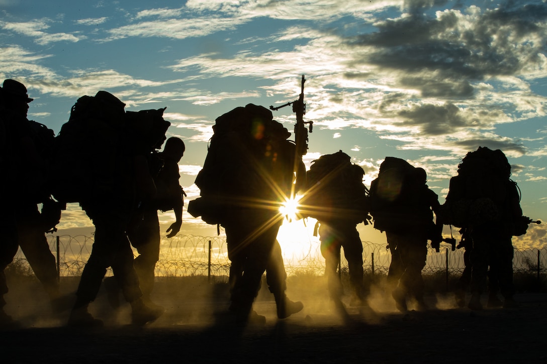 A group of Marines walk together with packs on their backs at twilight.
