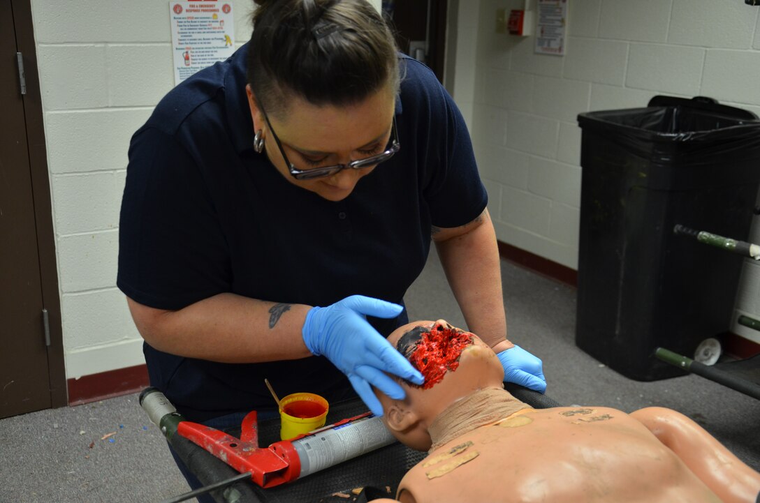 Camille Espinoza, a civilian Department of Combat Medic Training program instructor and simulations technician at the Medical Education and Training Campus at Joint Base San Antonio-Fort Sam Houston, applies red paint on the face on a low-fidelity manikin to create a realistic facial wound. Espinoza uses moulage to transform manikins into combat casualties to simulate battlefield wounds or injuries to train combat medics.