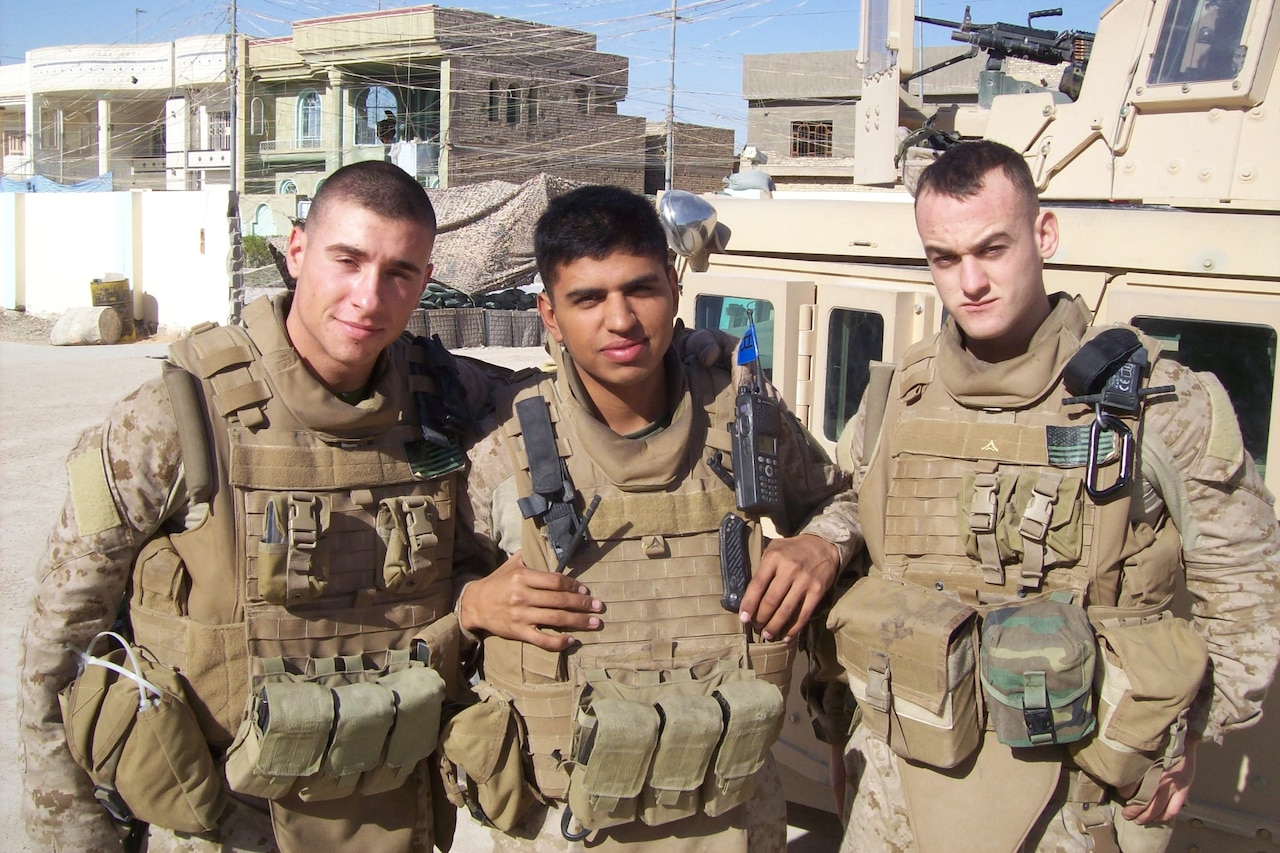 Three Marines in combat gear pose for a photo against a dusty, remote-looking landscape.