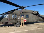 1LT Hollianne M. Peal stands in front of a UH-60 Blackhawk helicopter on a landing pad.