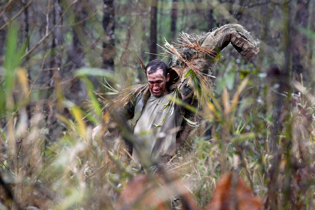 A soldier puts on his ghillie suit after adding natural vegetation.