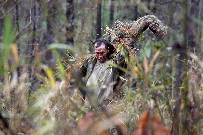 A soldier puts on his ghillie suit after adding natural vegetation.