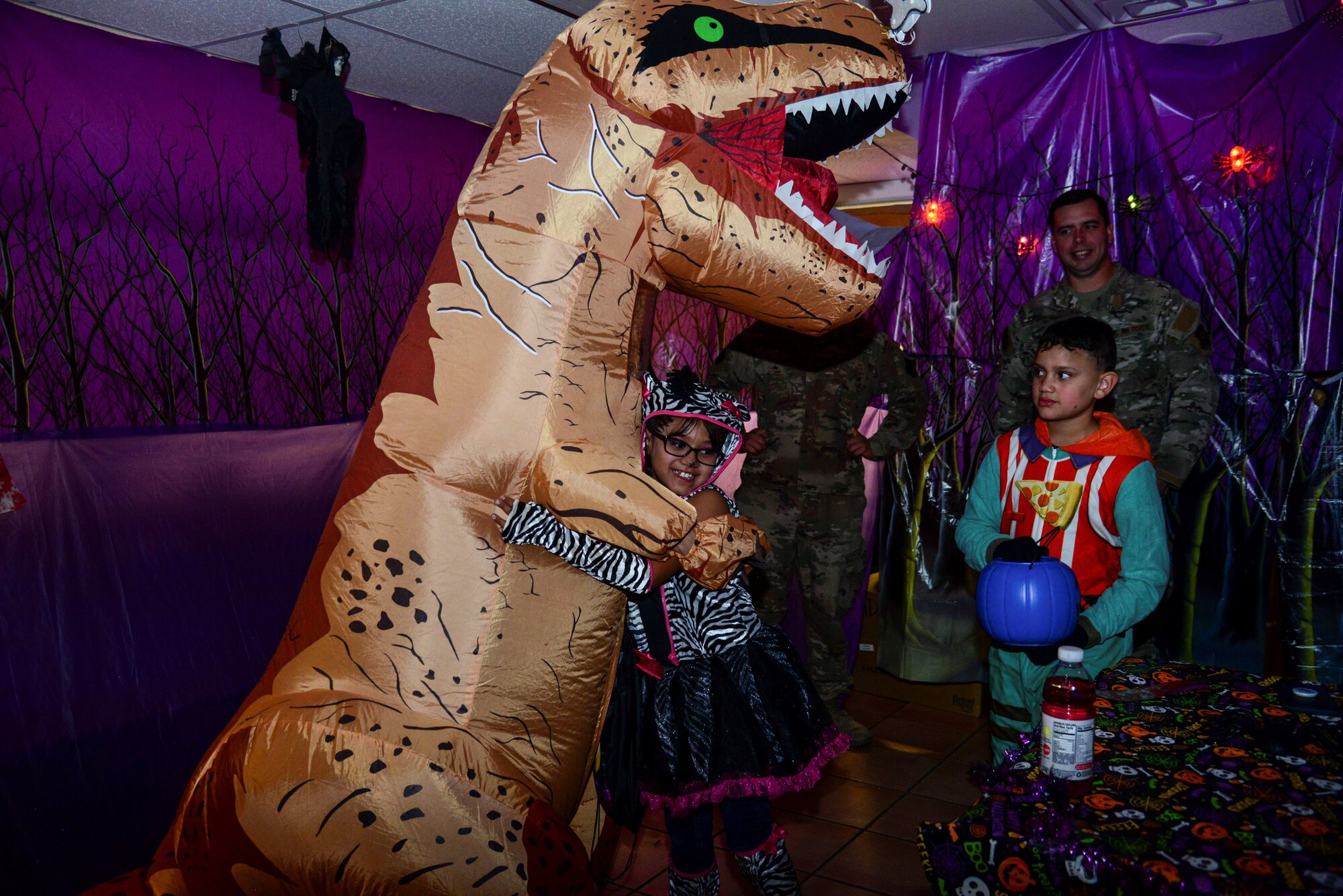 A Kirtland Elementary School student hugs a costumed dinosaur after receiving candy during a trick-or-treat event on Kirtland Air Force Base, N.M., Oct. 31, 2019. Each year, SMC invites the school to their Haunted Halloween event in which the entire building is filled with spooky decorations and hundreds of pounds of candy are passed out to costumed visitors.