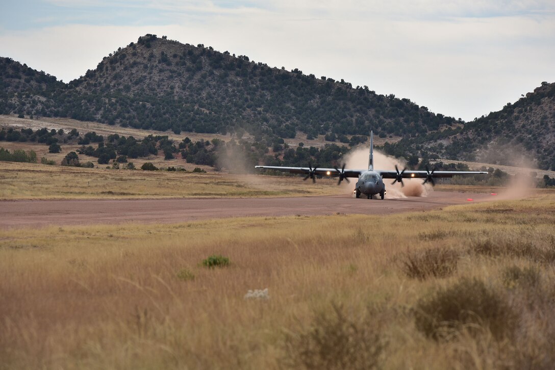A C-130 Hercules lands on a dirt runway.