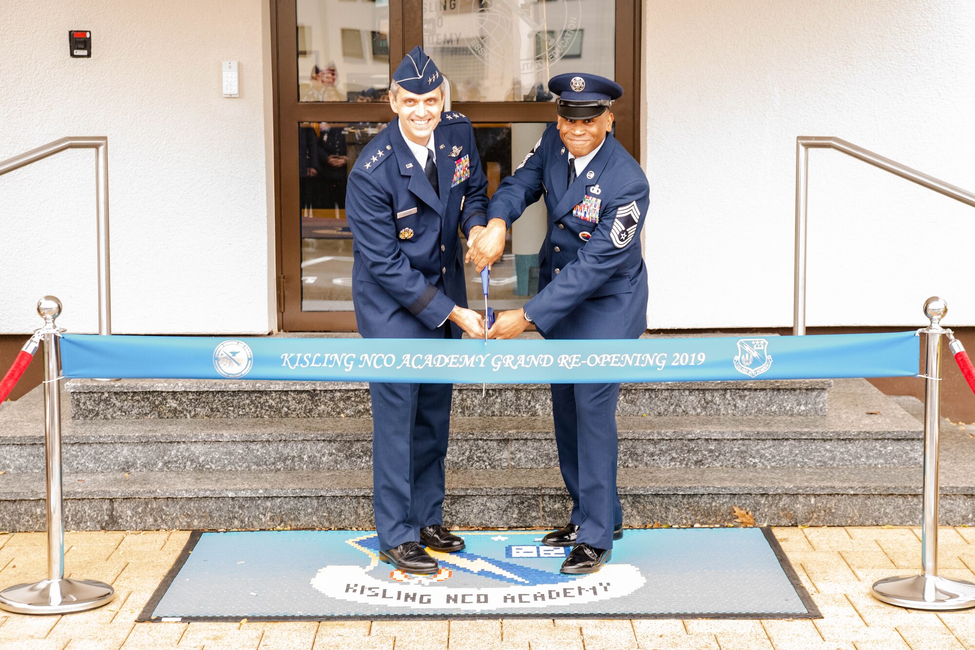 U.S. Air Force Lt. Gen. Steven L. Basham, United States Air Forces in Europe – Air Forces Africa deputy commander, and Chief Master Sgt. Terrance Smiley, Kisling Noncommissioned Officer Academy commandant, prepare to cut a ribbon for the NCOA’s reopening on Kapaun Air Station, Germany, Nov. 1, 2019. The NCOA underwent extensive renovations to update the building, restrooms, classrooms, and offices, allowing students and instructors to better focus on professional military education. (Courtesy Photo)