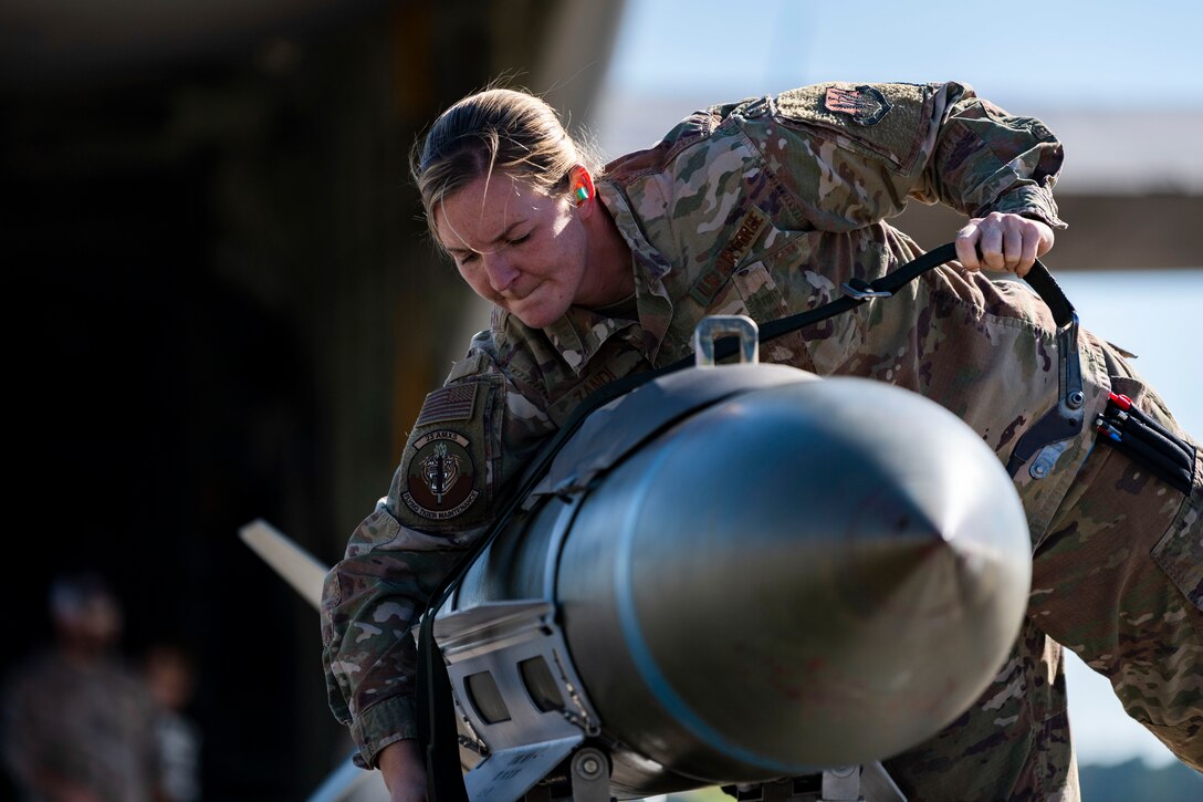 An airman tightens a rope on a large weapon.