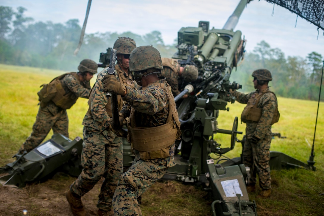 A group of Marines load ammunition into a large weapon.